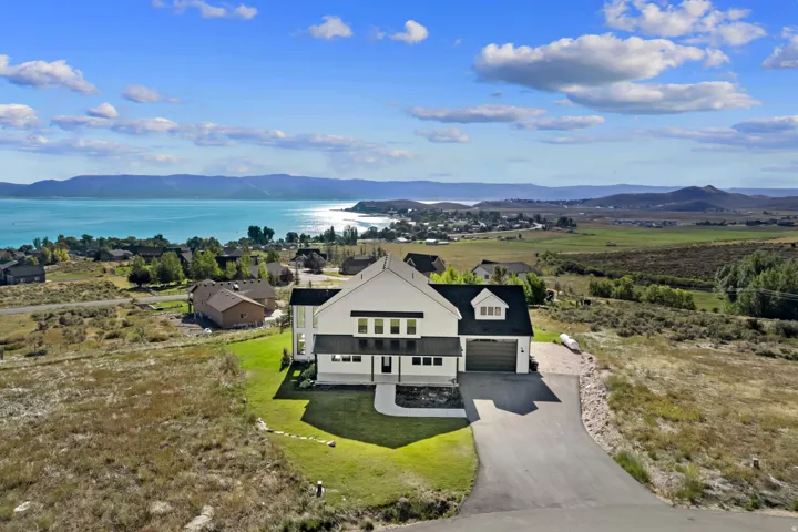 Modern white exterior with dark trim accents, a two-car garage, and a paved driveway, set against a backdrop of a large body of water and distant mountains