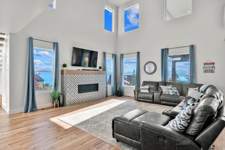 Vaulted ceilings, wood-finish flooring, patterned tile fireplace surround, linear electric fireplace, and a light-filled interior