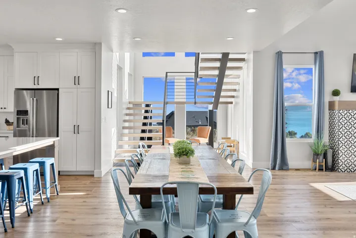 Open-concept interior featuring light wood-finish flooring, white shaker cabinetry, stainless steel refrigerator, and a modern open-tread staircase