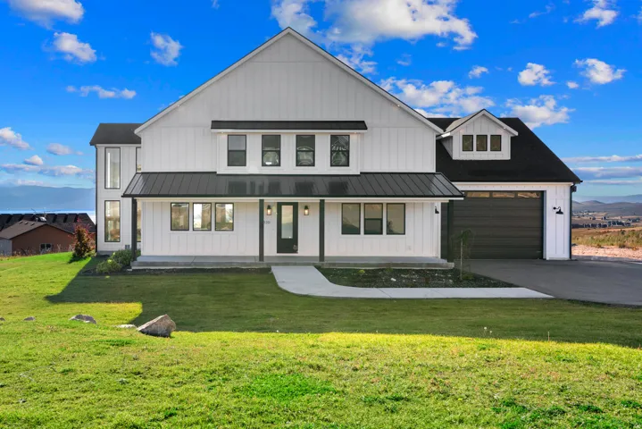 Board-and-batten siding with dark trim accents, covered porch with recessed lighting, black metal roof over the porch, attached garage with a dark door, and a concrete driveway