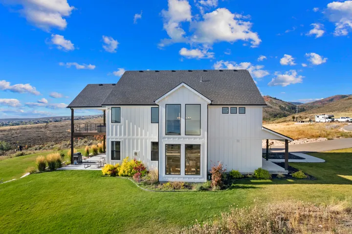 Modern farmhouse exterior with white board and batten siding, multiple large windows, a dark shingle roof, a second-story balcony with metal railings, and a concrete patio