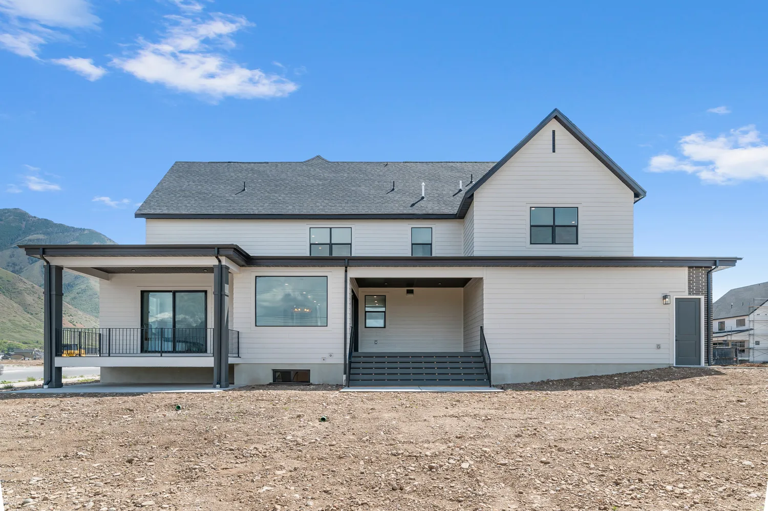 Contemporary exterior with white siding, covered patio with black railing, large fixed-pane window, and a gabled roofline