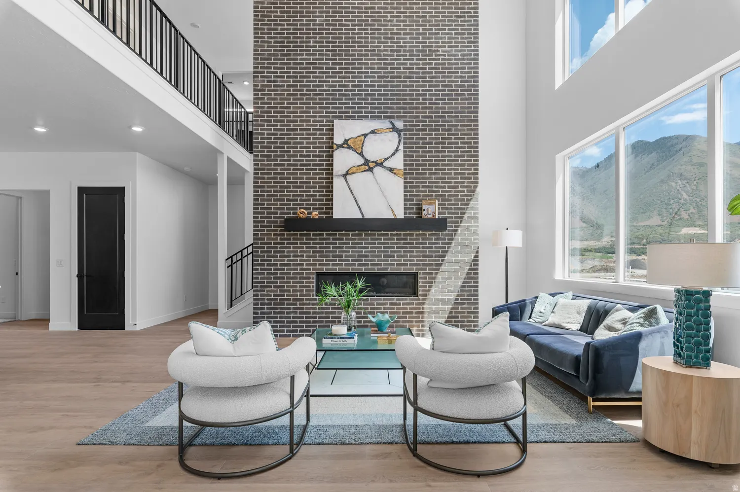 Two-story living area featuring a brick-clad fireplace, built-in linear fireplace, wood-finish flooring, and a second-story open-concept hallway with metal railings