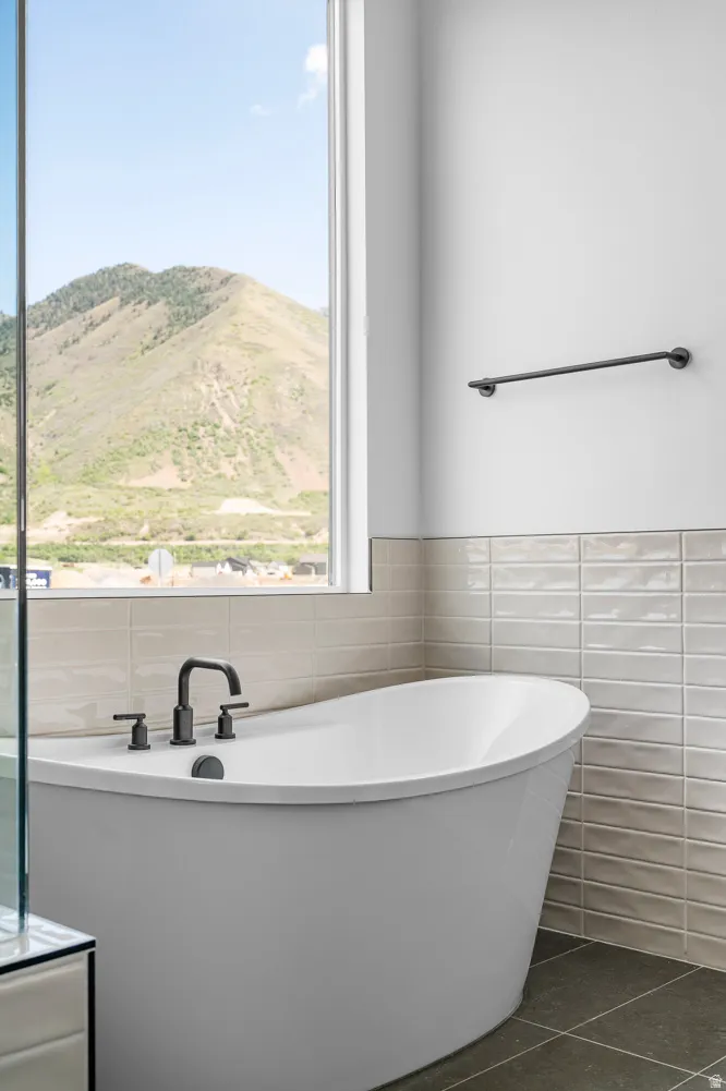 Freestanding soaking tub with matte black fixtures, set against a tiled wall and large window