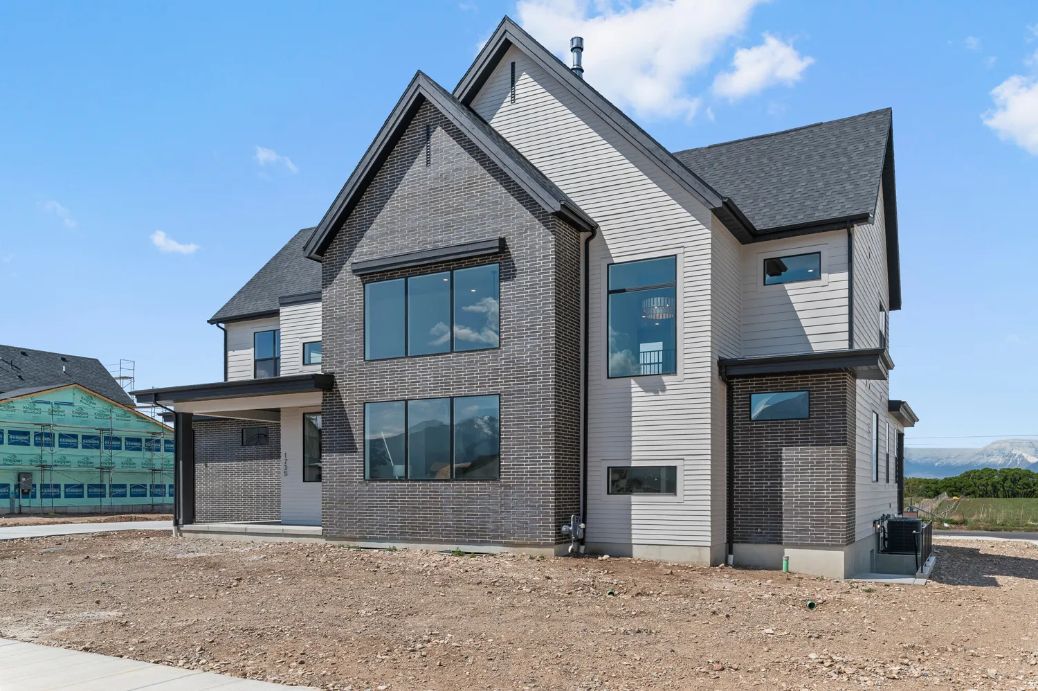 Modern two-story residence featuring a dark brick and light siding exterior, large black-framed windows, and a covered entry