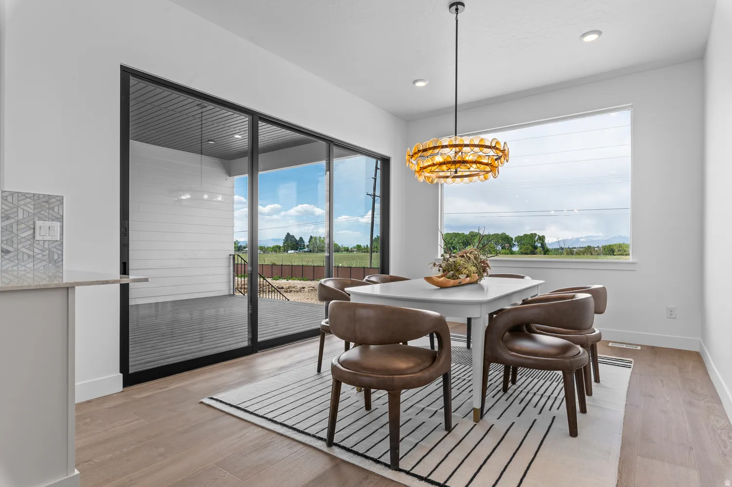 Bright dining area featuring wood-finish flooring, a contemporary chandelier, a large window, and sliding glass doors opening to an outdoor patio