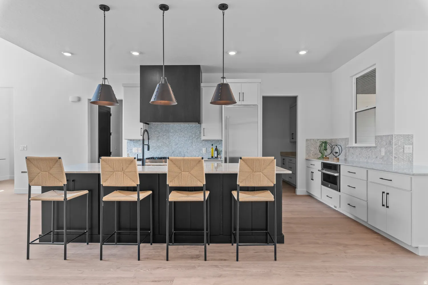 Spacious kitchen featuring a large island with pendant lighting, light wood-finish flooring, white cabinetry, and integrated appliances