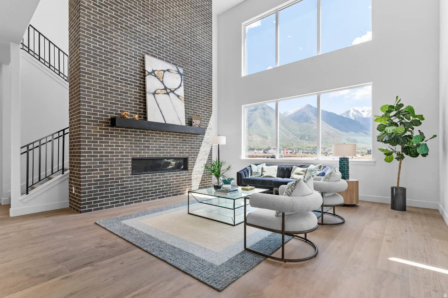 Two-story living area featuring wood-finish flooring, a full-height brick fireplace, a built-in linear fireplace, and floor-to-ceiling windows