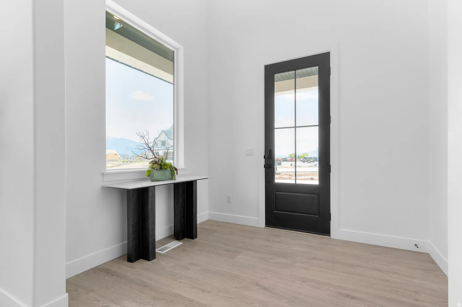 Crisp white walls, wood-finish flooring, and a black-framed glass-paneled entry door