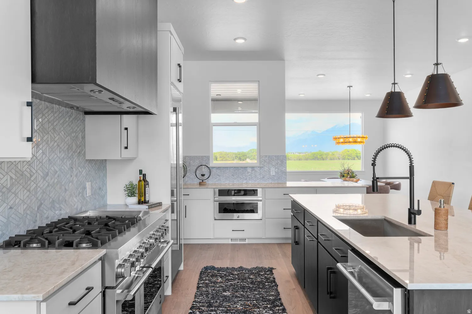 Gourmet kitchen with professional-grade stainless steel range, custom range hood, geometric tile backsplash, and an expansive island featuring an undermount sink and gooseneck faucet