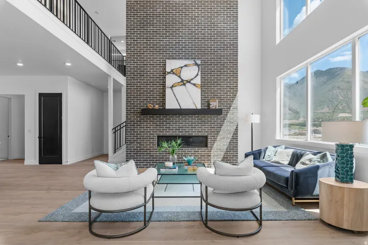 Two-story living area featuring a brick-clad fireplace, built-in linear fireplace, wood-finish flooring, and a second-story open-concept hallway with metal railings