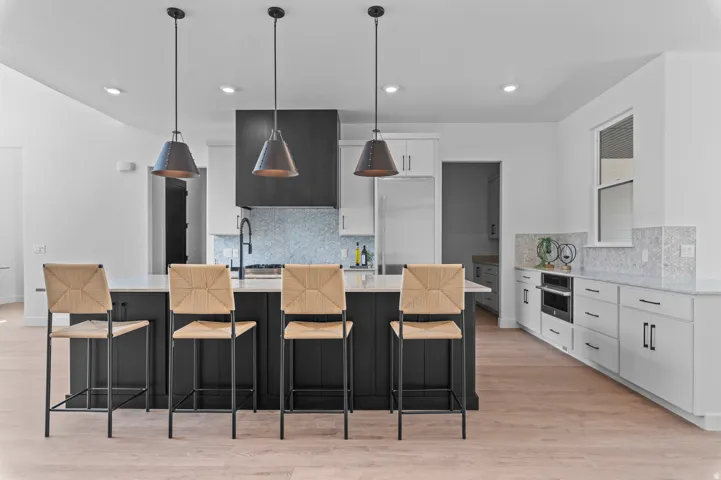 Spacious kitchen featuring a large island with pendant lighting, light wood-finish flooring, white cabinetry, and integrated appliances