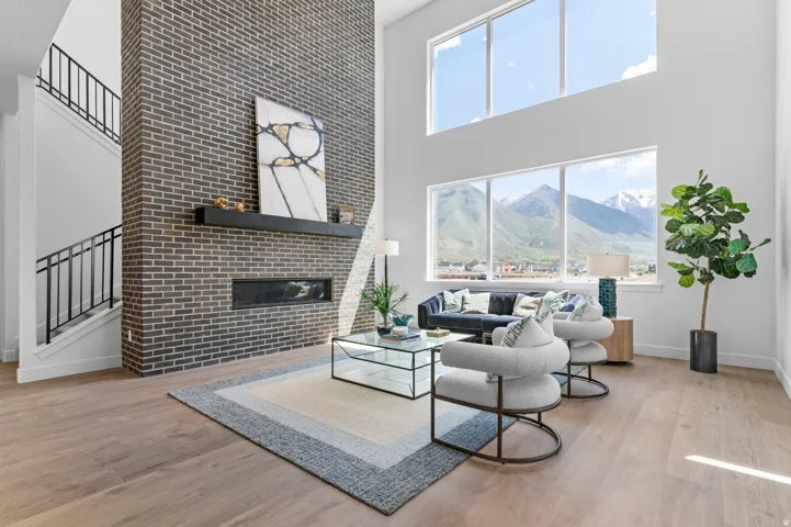 Two-story living area featuring wood-finish flooring, a full-height brick fireplace, a built-in linear fireplace, and floor-to-ceiling windows