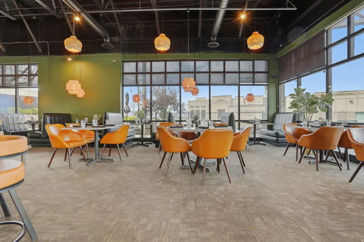 Expansive commercial interior featuring large industrial-style windows, exposed ceiling ducts, recessed lighting, and patterned commercial-grade carpeting