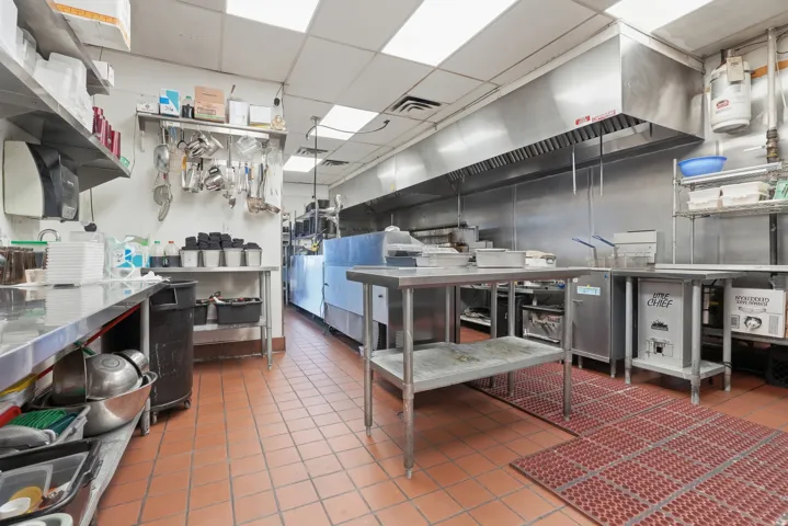 Commercial kitchen featuring extensive stainless steel workstations, a large exhaust hood, and tiled flooring
