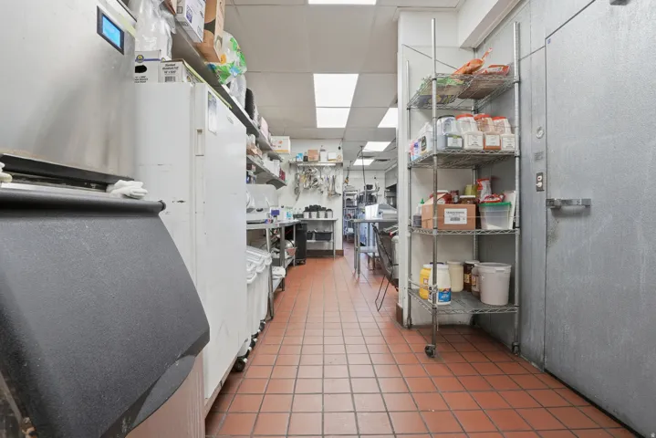 Commercial kitchen area featuring terra cotta-toned tile flooring, stainless steel appliances, and extensive shelving for storage