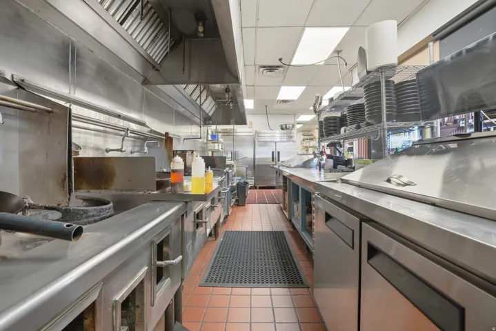 Professional kitchen with stainless steel countertops, industrial-grade range hood, and integrated under-counter refrigeration