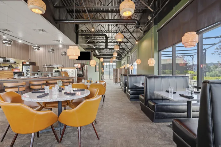 Exposed ceiling beams with industrial-style lighting, large windows, banquette seating, and a built-in service counter with bar stools