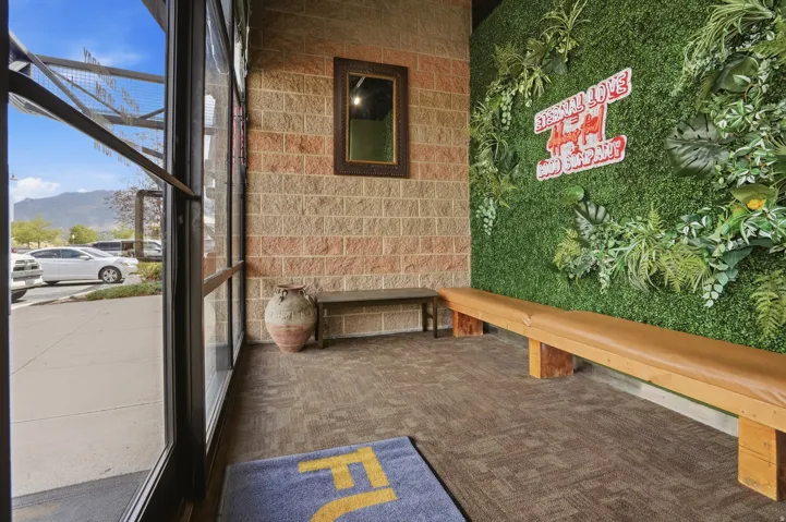 Glass-paned entry door with a dark frame, brick-finish wall, and a green wall feature with foliage