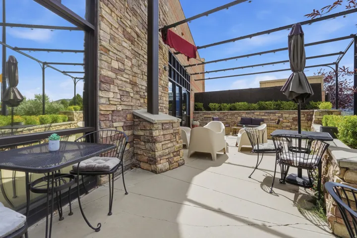 Outdoor patio featuring a stone-clad exterior, full-height windows, a metal pergola structure, and a concrete surface