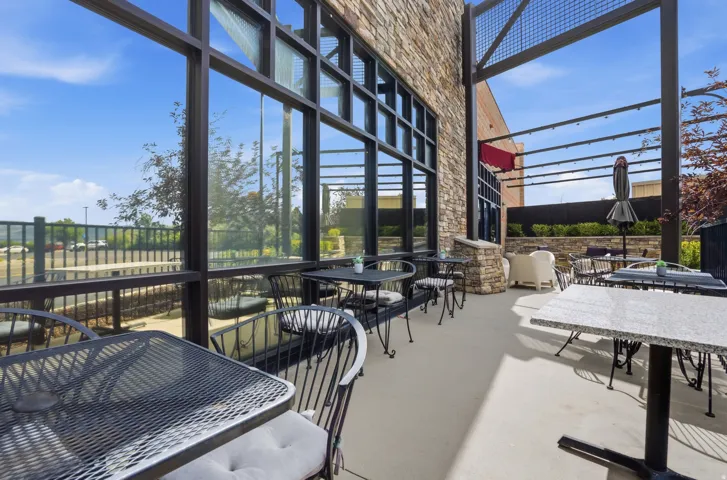 Stone-clad exterior with large framed windows, concrete patio, and an open metal pergola structure