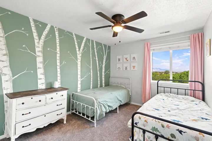 Accent wall with tree motif, ceiling fan with integrated lighting, window with mountain backdrop, neutral wall color, and carpeted flooring
