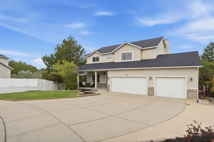 Stucco exterior with stone accents, covered front porch, two-car garage with individual doors, concrete driveway, and front lawn