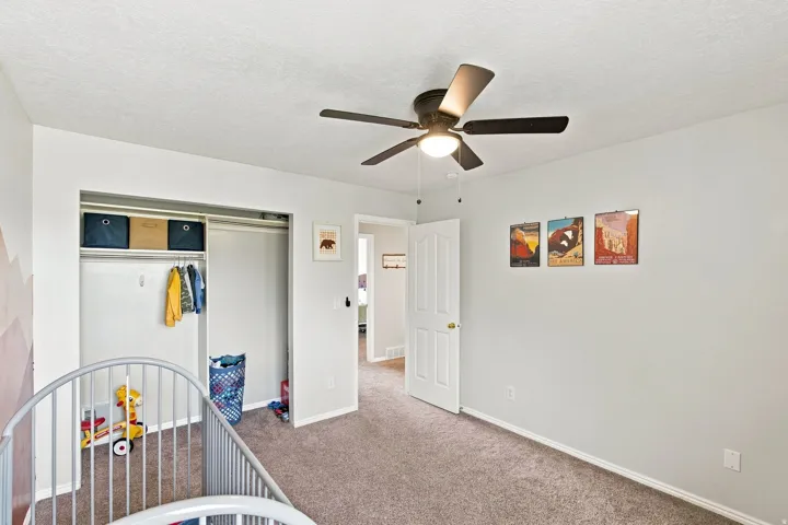 Neutral wall paint, carpeting, a ceiling fan with integrated lighting, a built-in closet with shelving and hanging rod, and a paneled interior door