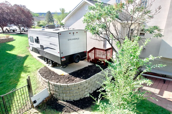 Paved RV pad, tiered retaining wall, manicured lawn, and exterior stairs