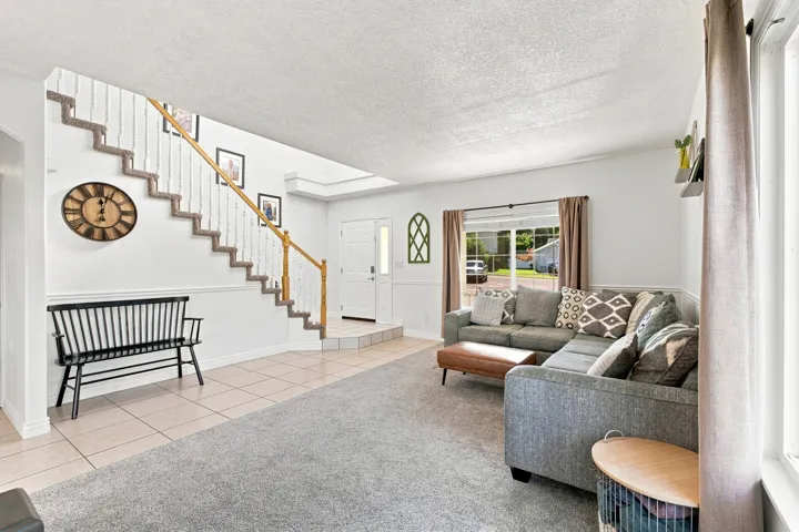 Open-concept living area with a carpeted staircase, tiled entry, and large window