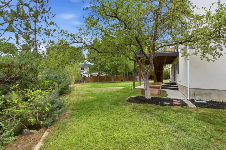 Expansive lawn area with mature trees, a raised deck, ground-level patio, and a well-defined garden bed