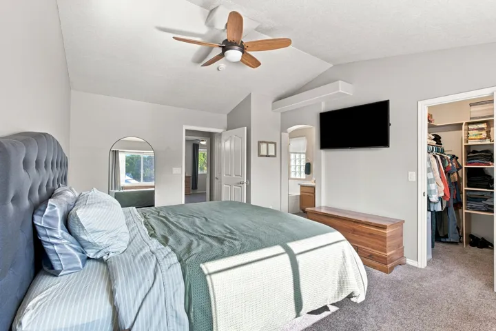 Vaulted ceiling with a wood-finish ceiling fan, wall-mounted television, and a built-in closet with shelving