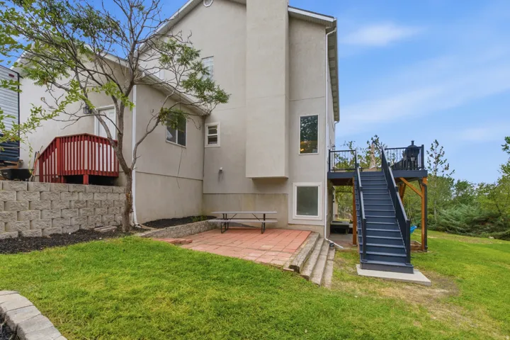 Stucco exterior with multiple windows, an upper-level deck with red railing, and a ground-level patio with brick pavers