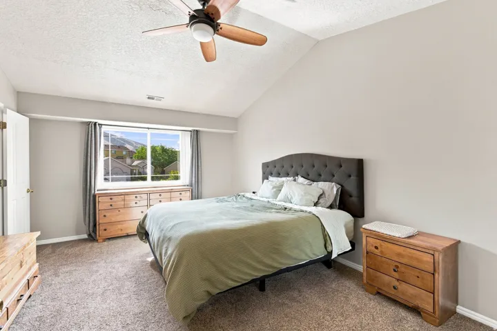Angled vaulted ceiling with a ceiling fan, light gray wall paint, and a large window