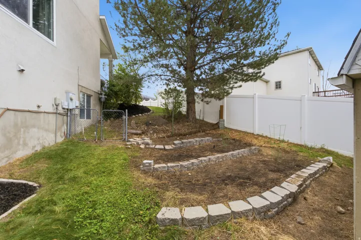 Expansive backyard with a mature tree, terraced garden beds, and white privacy fencing