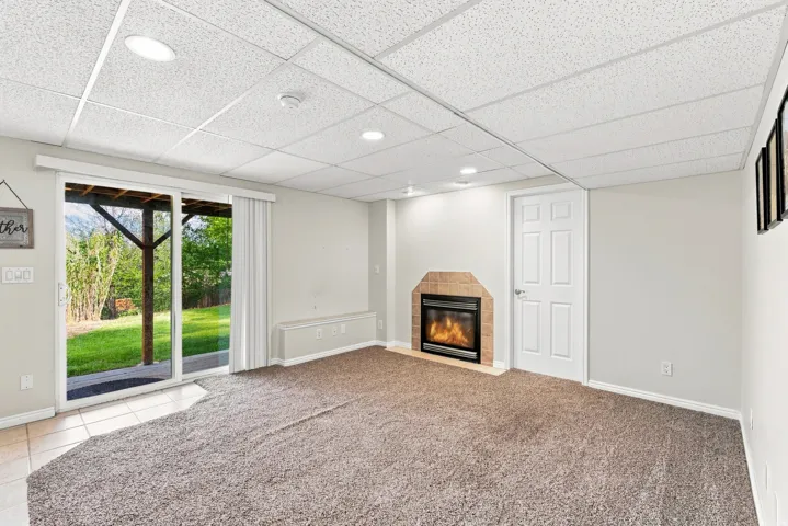 Recessed lighting, drop ceiling, gas fireplace with brick surround, sliding glass door to exterior, and carpeted flooring