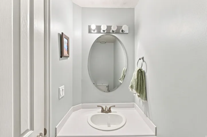 White built-in vanity with an undermount sink and brushed nickel faucet, complemented by an oval mirror and a four-bulb vanity light fixture
