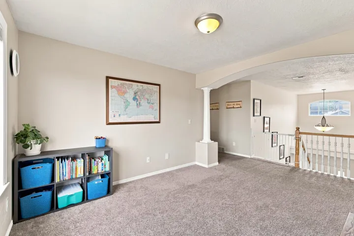 Carpeted upper-level space featuring an arched entryway with a decorative column, a window, and a staircase with a wood handrail and white balusters