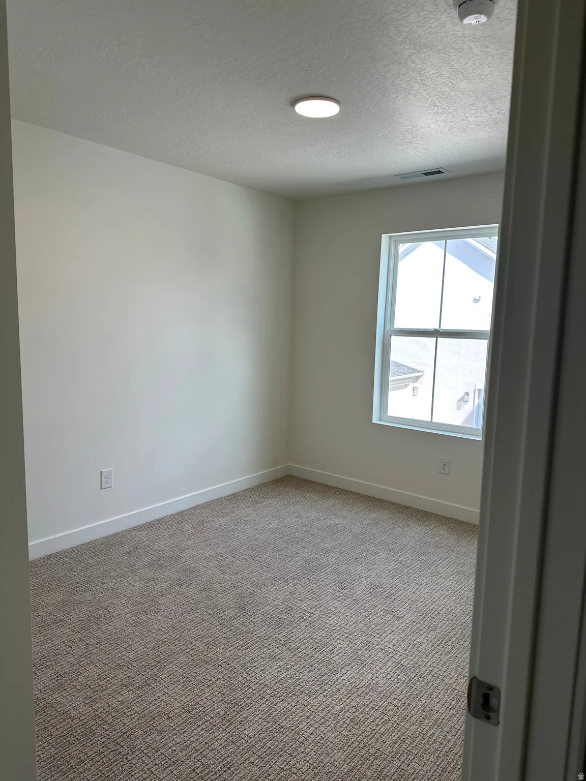 Recessed lighting, neutral wall paint, textured carpet, and a window with white trim