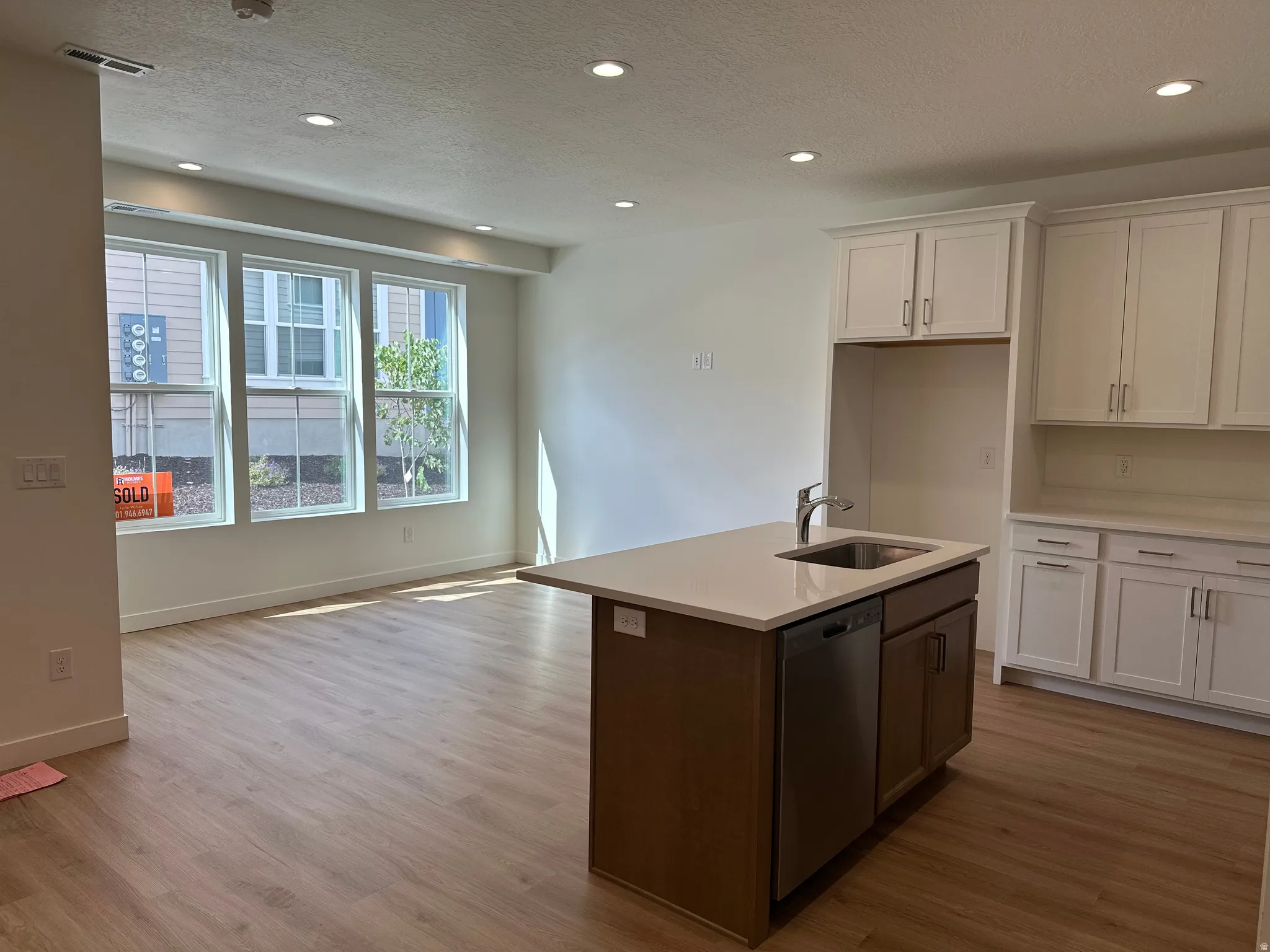 Kitchen island with undermount sink and stainless-steel dishwasher, quartz countertops, white upper and lower cabinetry, wood-finish flooring, and recessed lighting