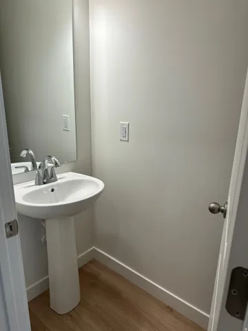 Pedestal sink with a chrome faucet, wall-mounted mirror, and wood-finish flooring