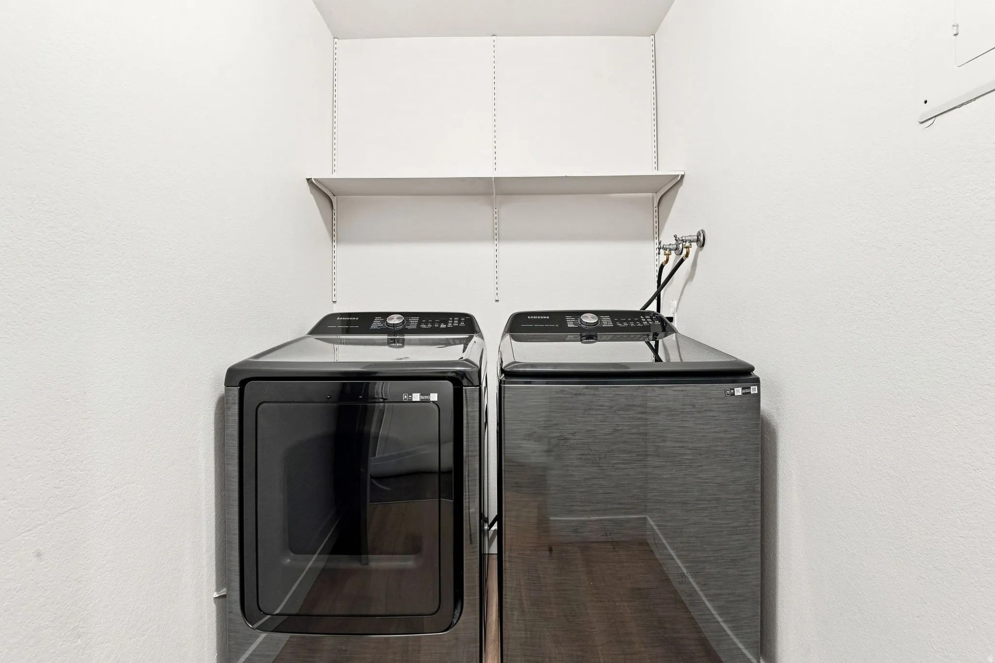 Dedicated laundry area with built-in shelving, wood-finish flooring, and white walls