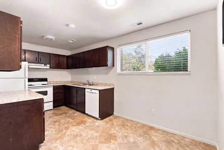Kitchen featuring wood-finish cabinetry, white appliances, and a window with blinds