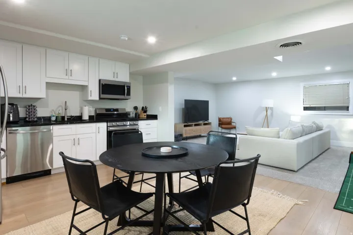Open-concept living area with wood-finish flooring, recessed lighting, and a kitchen featuring white cabinetry, black countertops, and stainless steel appliances