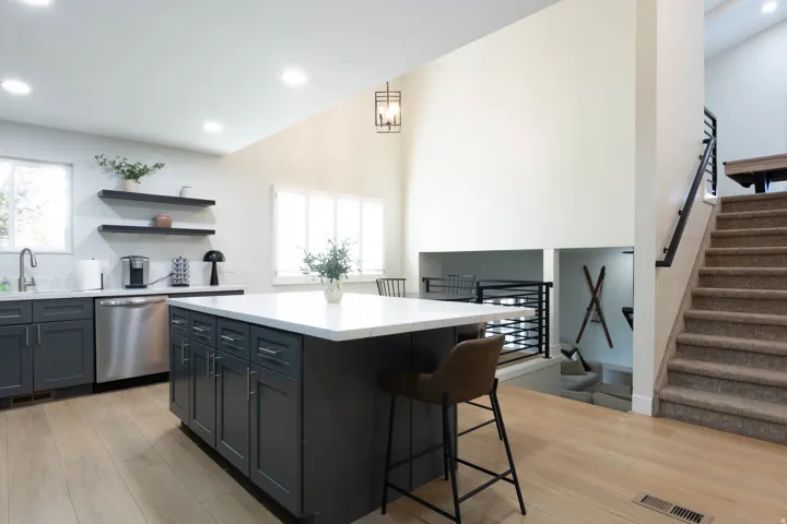 Kitchen featuring an island with white countertop, dark cabinetry, stainless steel appliances, and wood-finish flooring