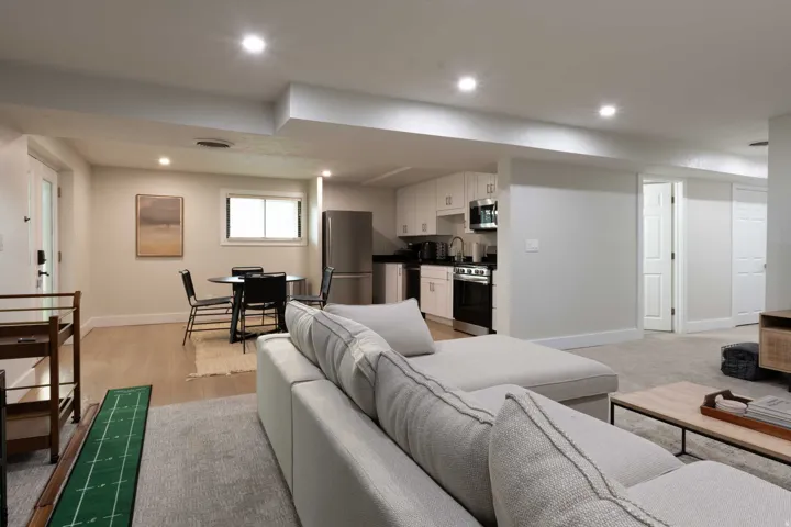 Recessed lighting illuminates the open living area, featuring a kitchen with white cabinetry and stainless steel appliances