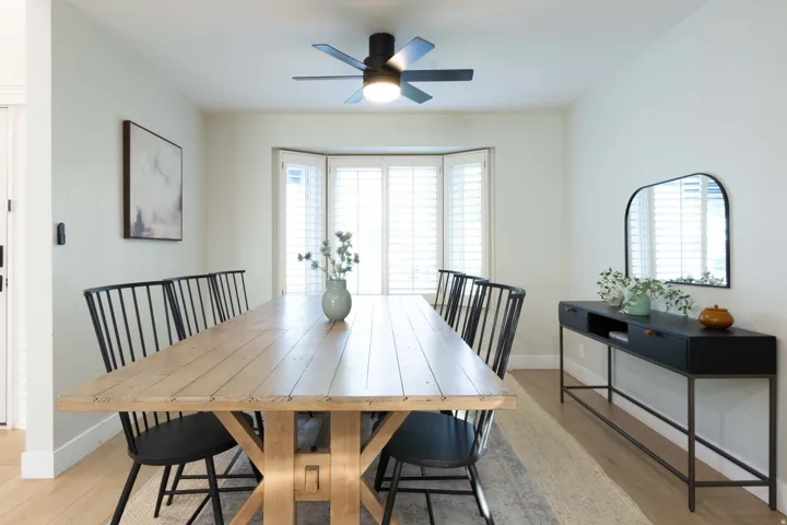 Recessed bay window with plantation shutters, overhead ceiling fan with lighting, wood-finish flooring, and neutral wall tones
