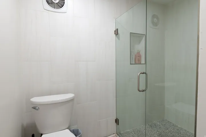 White tile walling with a built-in shower niche, glass-enclosed shower, and a pebble-finish shower floor