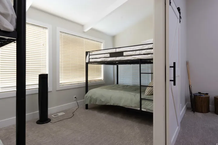 Vaulted ceiling with exposed beam, dual windows with blinds, and light gray wall paint
