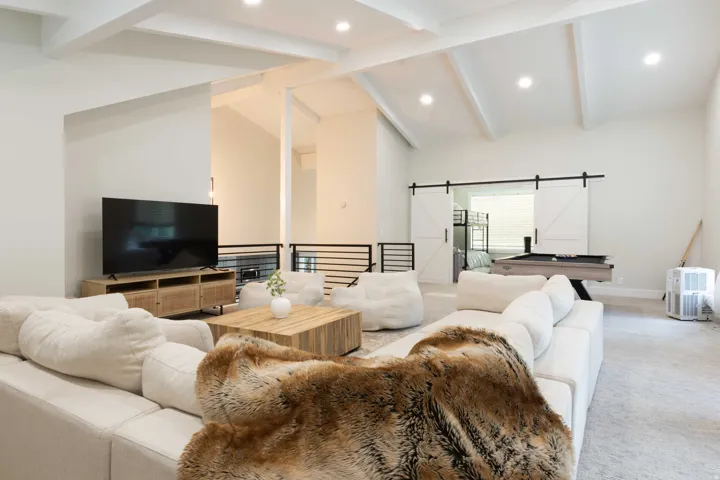 Vaulted ceiling with exposed beams, recessed lighting, white barn doors, and metal railing